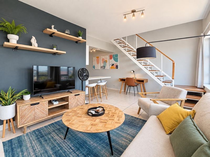 Modern open-plan living area featuring a striking dark accent wall with floating shelves, tiled flooring, and a contemporary staircase with wooden treads.