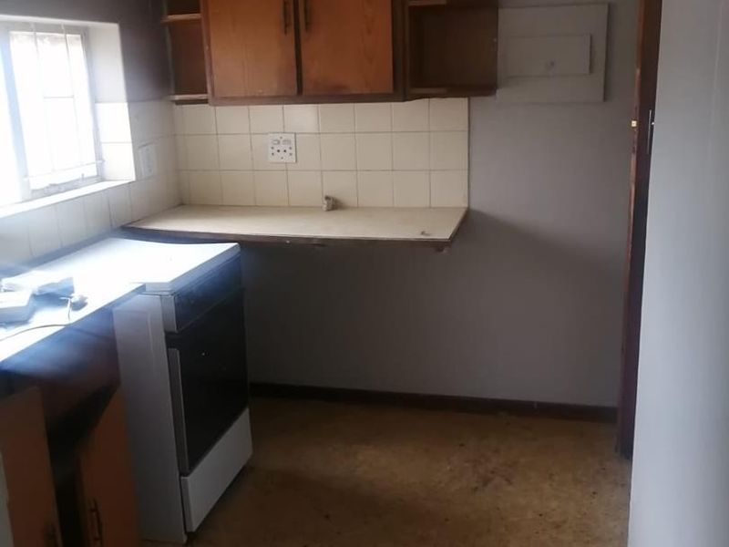 A dated, empty kitchen featuring original wooden cabinetry, a tiled backsplash, and a freestanding stove, requiring modernization and floor repairs.