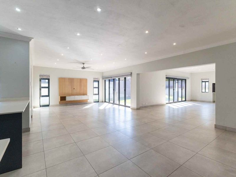 Spacious open-plan living area featuring large format floor tiles, recessed lighting, and multiple aluminium sliding doors providing seamless access to the outdoor space.