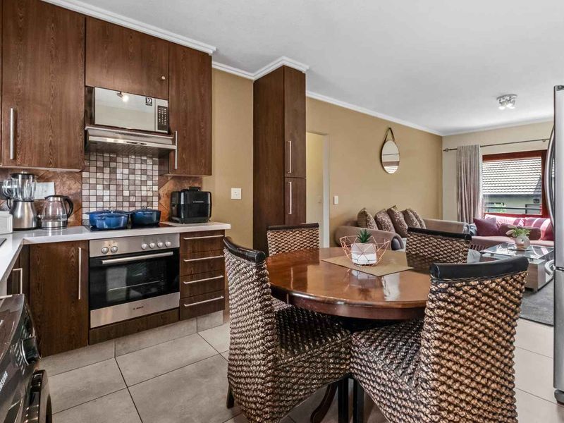 Open-plan kitchen and living area featuring dark wood cabinetry, mosaic tile backsplash, and tiled flooring, creating a functional and connected living space.