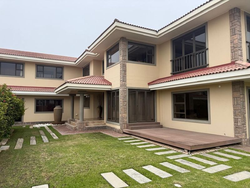 Rear view of a multi-level house featuring a timber deck, stone-clad accents, terracotta roof tiles, and a landscaped garden with a stone walkway.