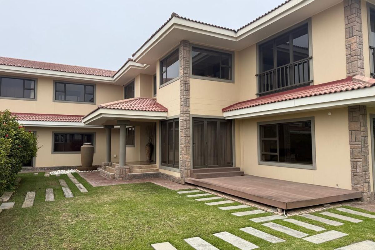 Rear view of a multi-level house featuring a timber deck, stone-clad accents, terracotta roof tiles, and a landscaped garden with a stone walkway.