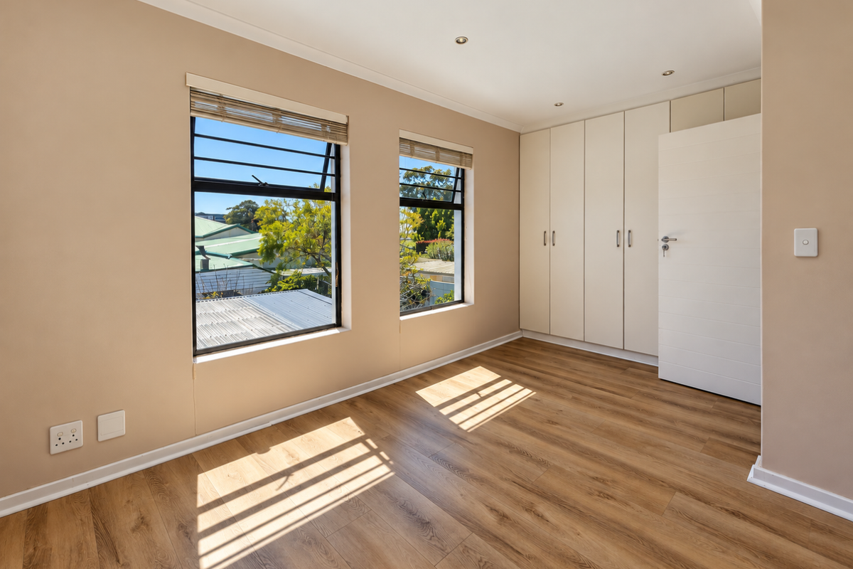 A bright and spacious bedroom featuring modern laminate flooring, built-in cupboards, and large windows that provide ample natural light.