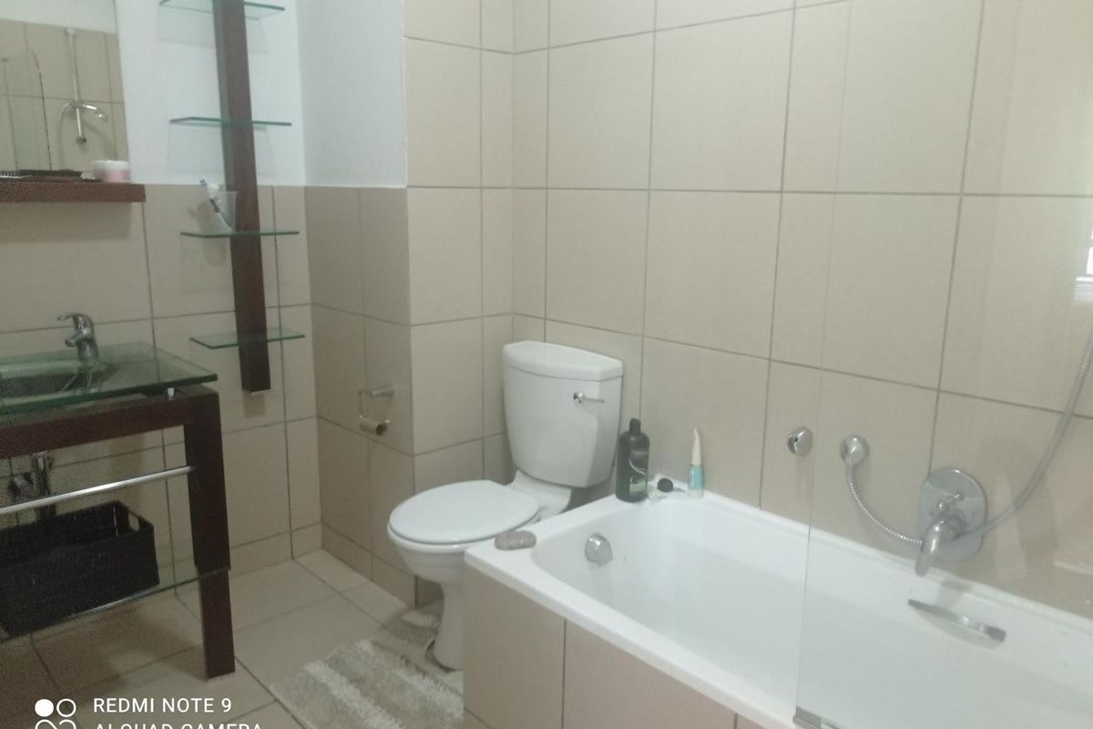 A functional bathroom featuring a glass vessel sink, wall-mounted shelving, a standard toilet, and a bathtub with a glass shower screen and tiled walls.