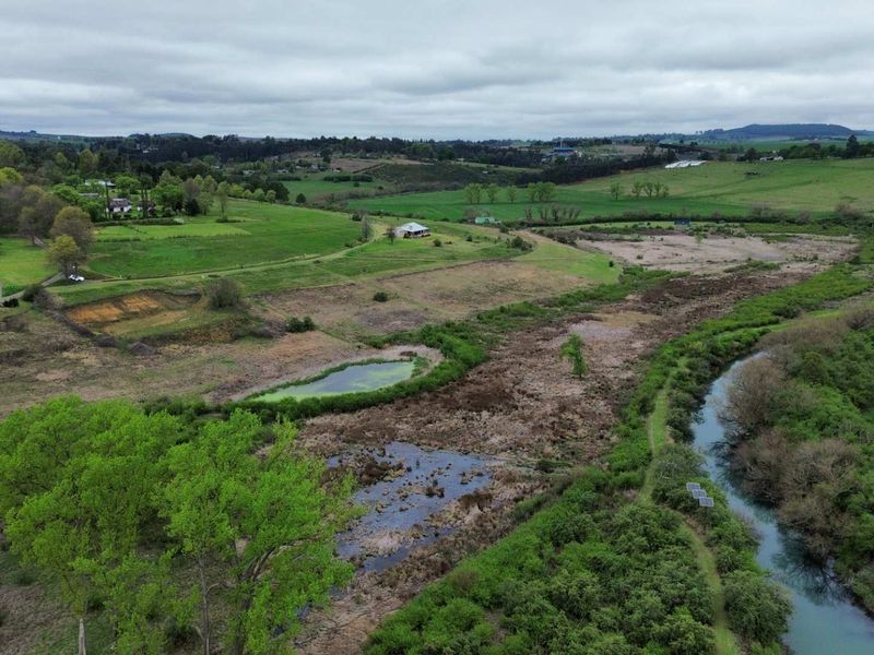 An aerial view of a large residential vacant land parcel featuring natural watercourses, wetlands, and expansive green pasture land in a rural setting.