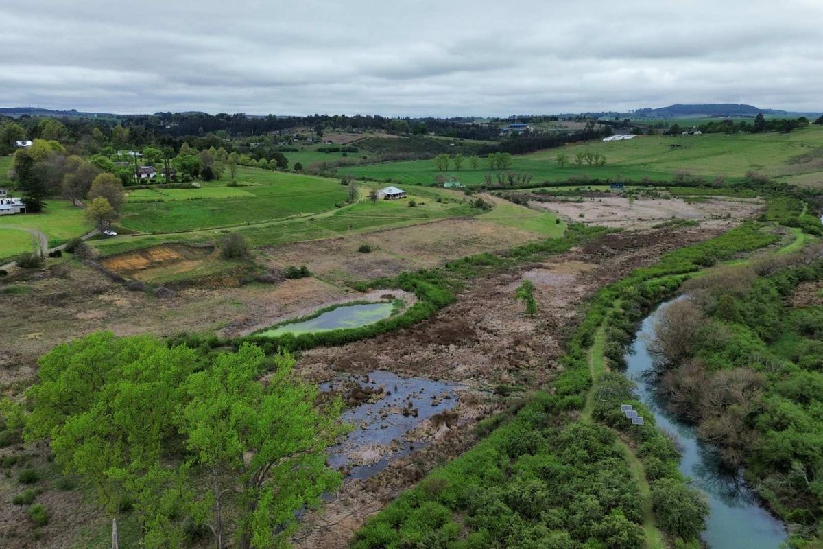 An aerial view of a large residential vacant land parcel featuring natural watercourses, wetlands, and expansive green pasture land in a rural setting.