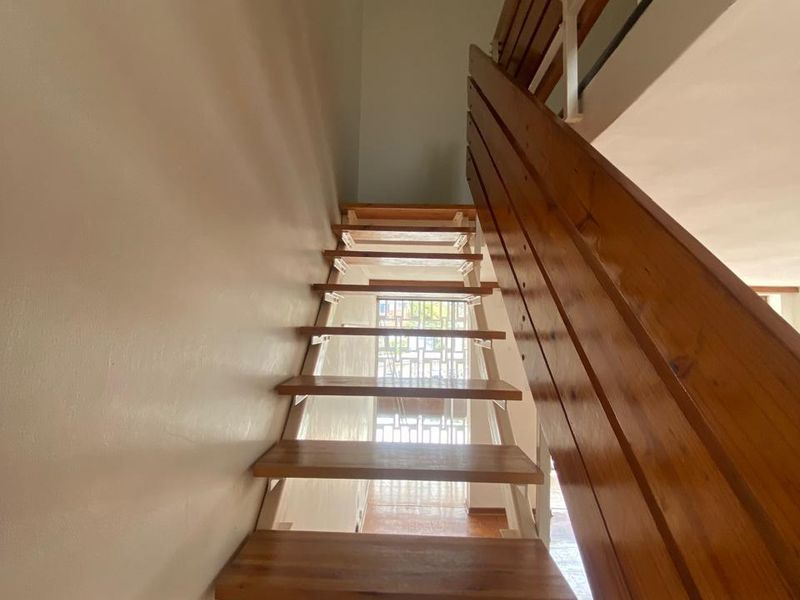 A staircase featuring timber treads and a matching timber handrail, leading towards a secure entrance gate.