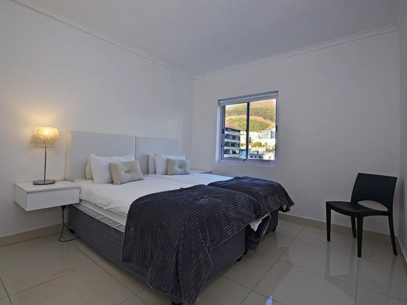 A bright bedroom featuring tiled flooring, a sliding window with exterior views, and clean white walls.