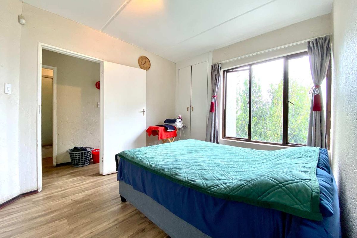 A bedroom featuring built-in cupboards, wood-look flooring, and a window with natural light, providing access to an adjacent room.
