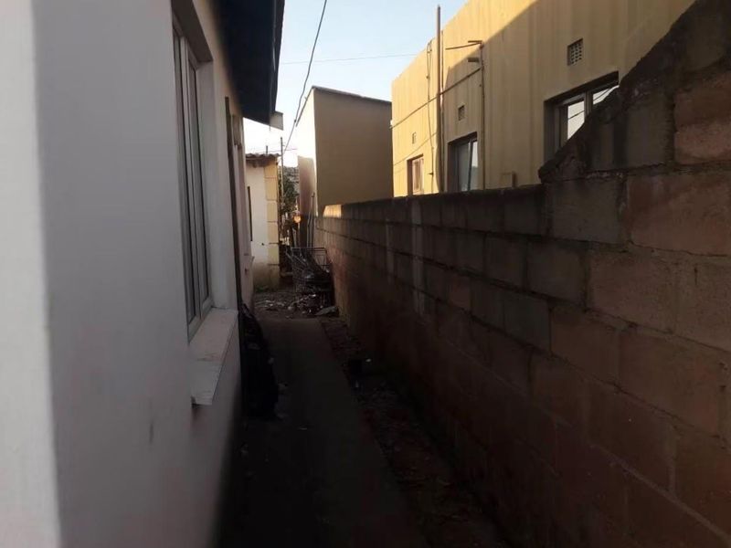 A narrow side passage between the property and a concrete block boundary wall, showing signs of wear and debris.