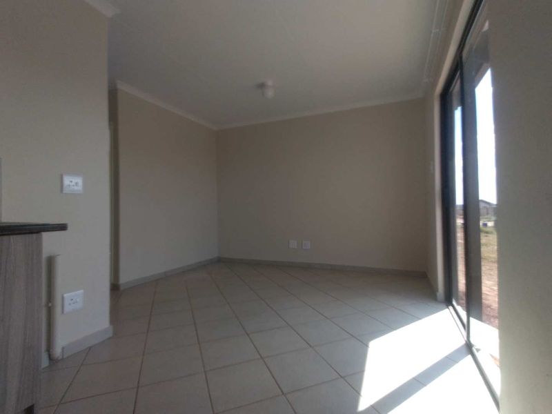A bright, empty open-plan living area featuring neutral tiled flooring and a large sliding glass door providing natural light and outdoor access.