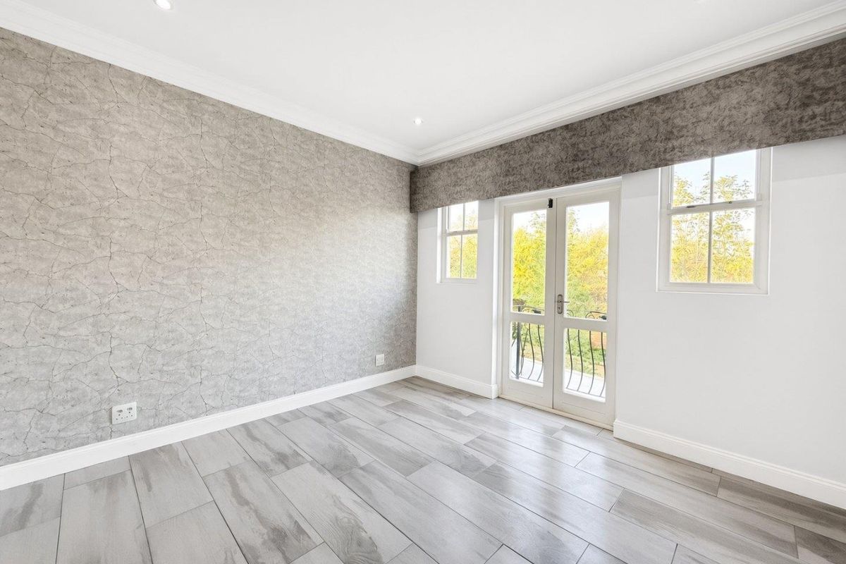 A bright, empty bedroom featuring modern tiled flooring, textured feature wallpaper, recessed lighting, and double french doors leading to a balcony.