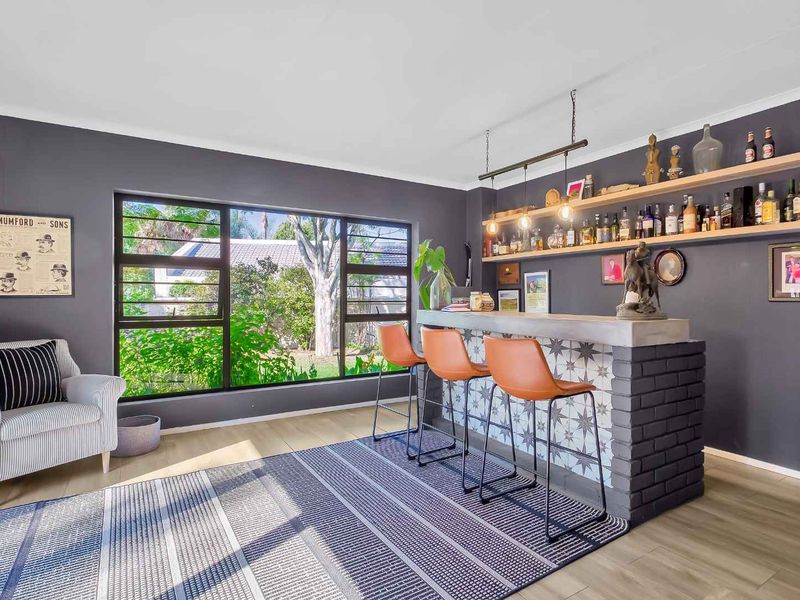 A stylish home bar area featuring a custom brick and tile counter, floating timber shelves, and large windows overlooking the garden.