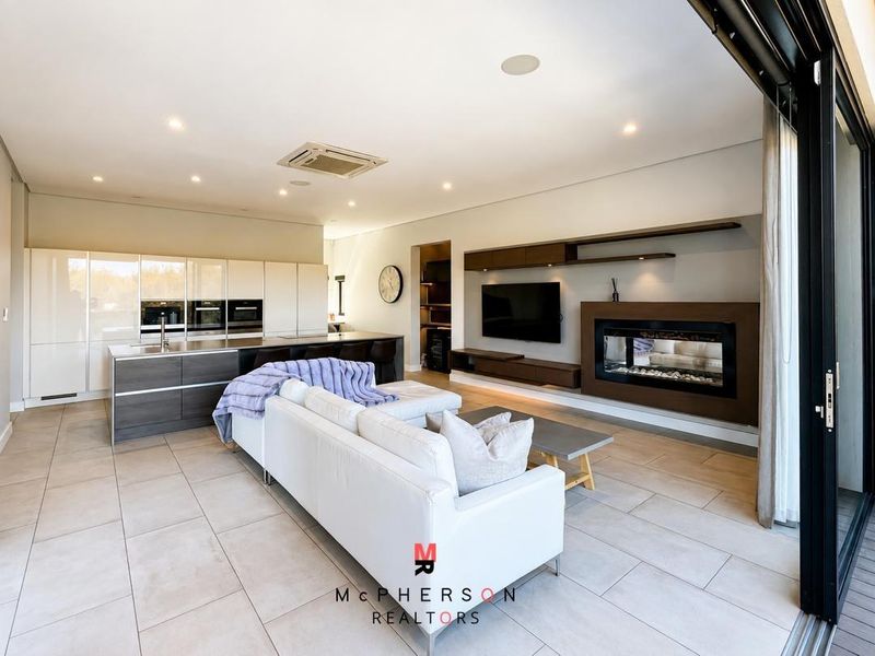 Modern open-plan living area featuring a sleek kitchen with integrated appliances, a built-in fireplace, and seamless flow to the outdoor patio.