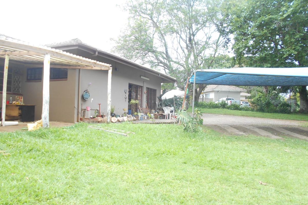 Rear view of the property featuring a covered patio area, paved driveway, and a shade cloth carport structure set within a garden.