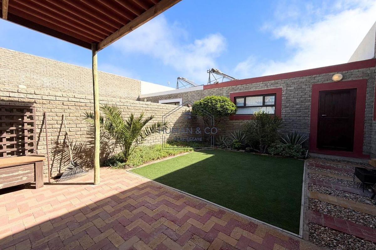 A private rear courtyard featuring a paved patio area, artificial lawn, perimeter brick walling, and a covered pergola structure.