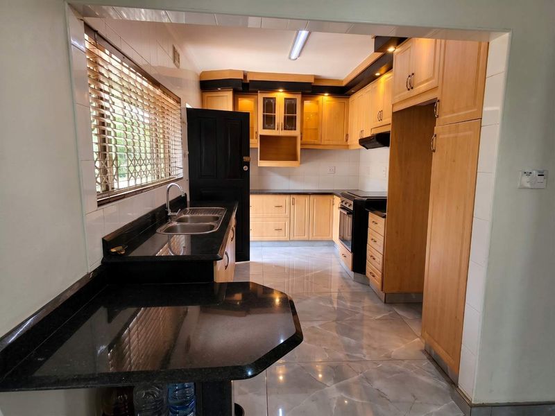 A functional kitchen featuring light wood cabinetry, dark granite countertops, a double basin sink, and built-in oven with extractor fan.