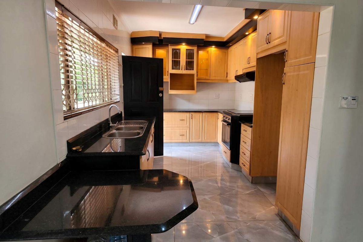 A functional kitchen featuring light wood cabinetry, dark granite countertops, a double basin sink, and built-in oven with extractor fan.