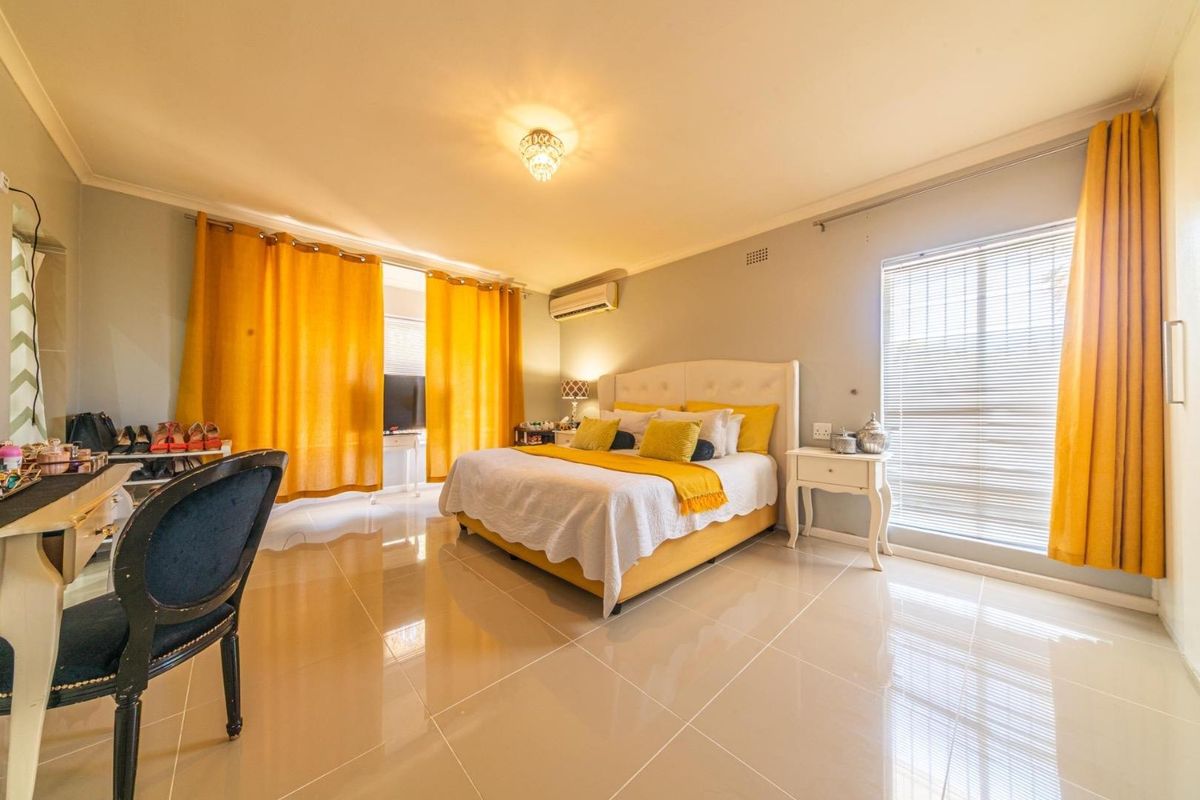 Spacious bedroom featuring polished tile flooring, a wall-mounted air conditioning unit, and large windows with integrated blinds.