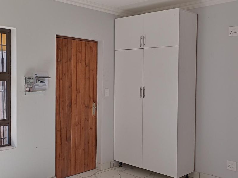 A clean, neutral bedroom featuring tiled flooring, a built-in wardrobe, and a secure window with burglar bars.