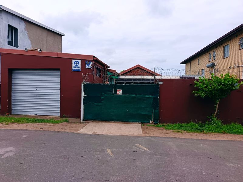 Front exterior view showing a roller shutter garage door, perimeter wall with security razor wire, and a gated entrance.