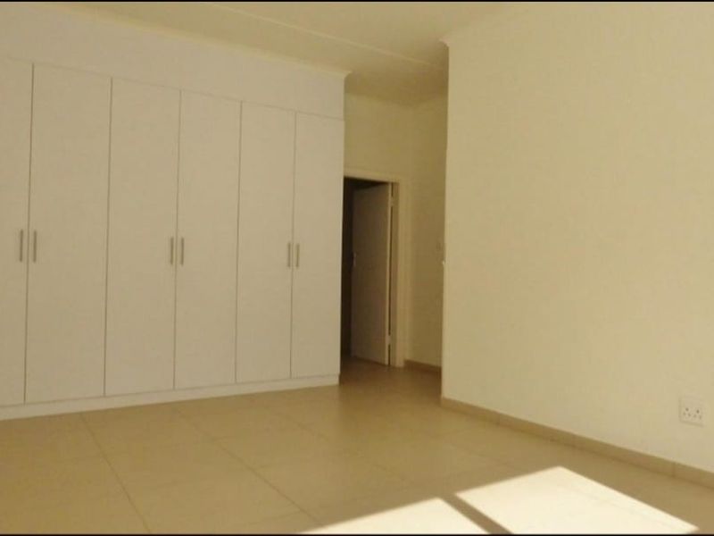 A clean, empty bedroom featuring neutral tiled flooring and extensive white built-in cupboards, offering a blank canvas for personalization.