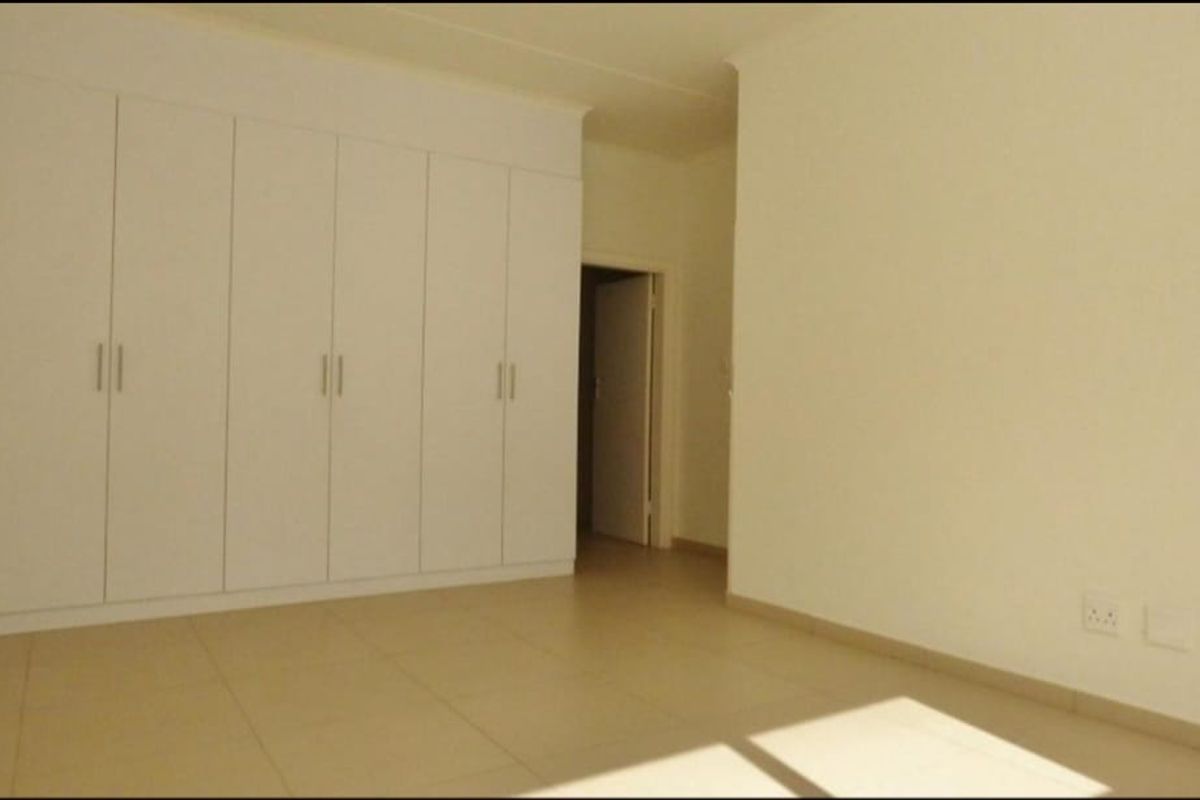 A clean, empty bedroom featuring neutral tiled flooring and extensive white built-in cupboards, offering a blank canvas for personalization.