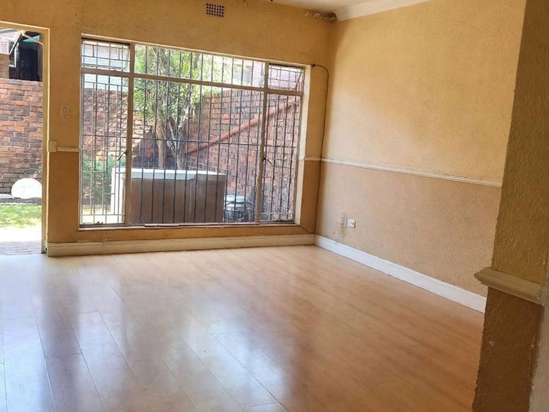 An empty living room featuring laminate flooring, a ceiling fan, and large windows with security bars, showing signs of wear and needing cosmetic updates.