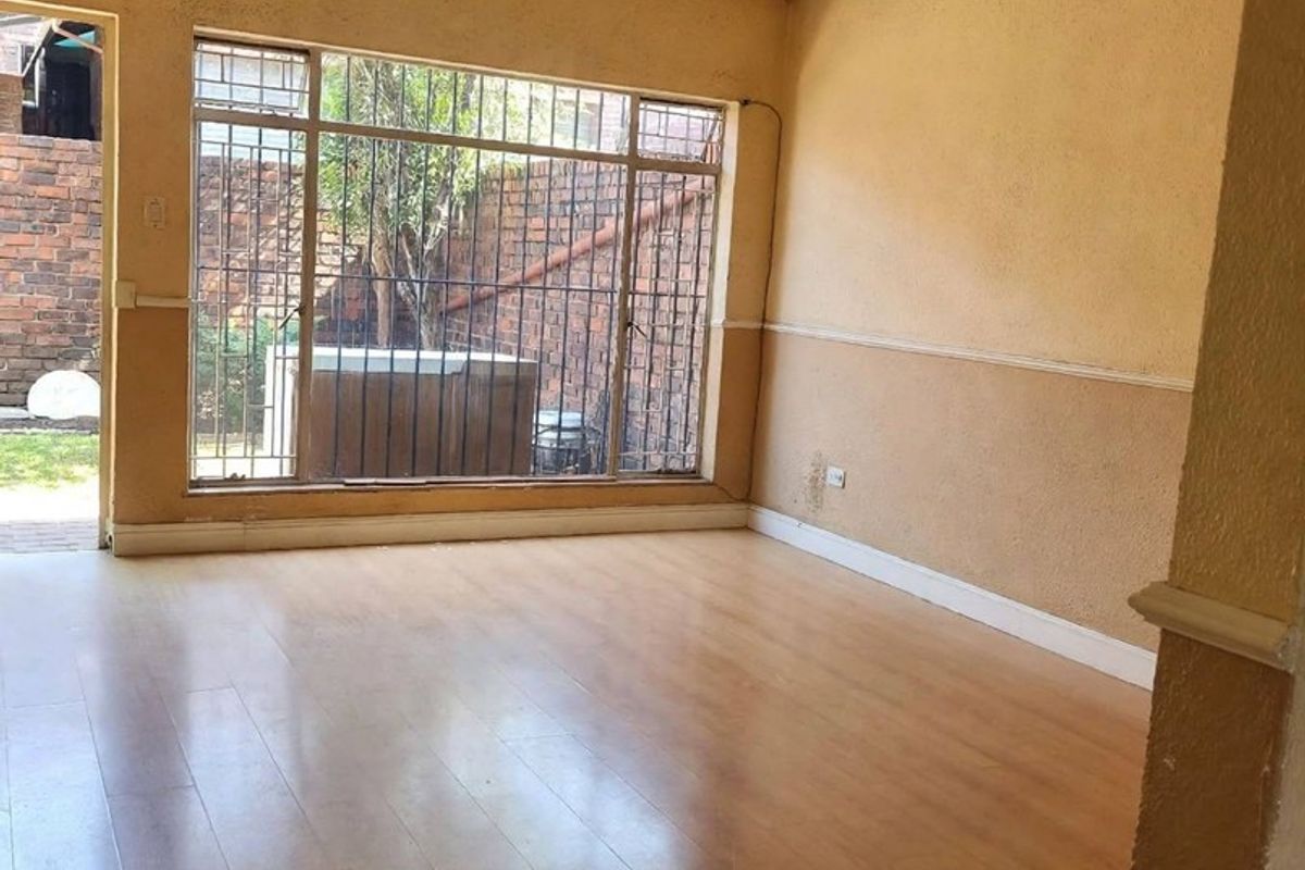 An empty living room featuring laminate flooring, a ceiling fan, and large windows with security bars, showing signs of wear and needing cosmetic updates.
