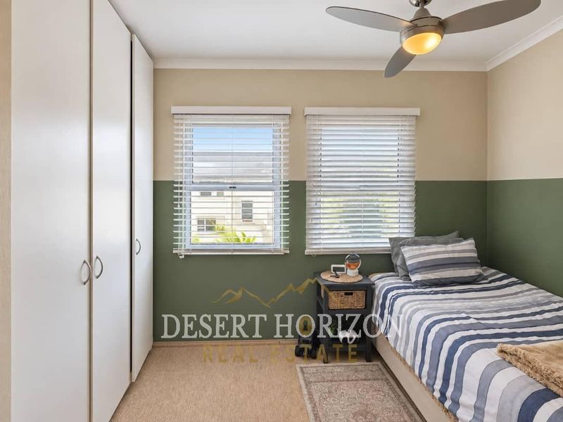A well-maintained bedroom featuring built-in wardrobes, a ceiling fan, and dual windows with venetian blinds, offering a comfortable and functional living space.