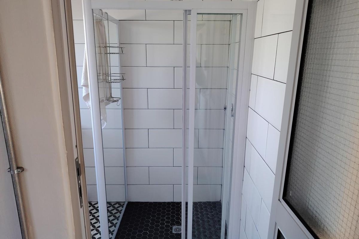 A clean, modern bathroom shower featuring white subway wall tiles and contrasting black hexagonal floor tiles with a glass enclosure.
