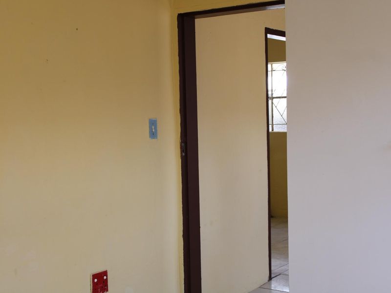 A view through a doorway into an adjacent room, showing plain interior walls and basic electrical fixtures in a vacant space.