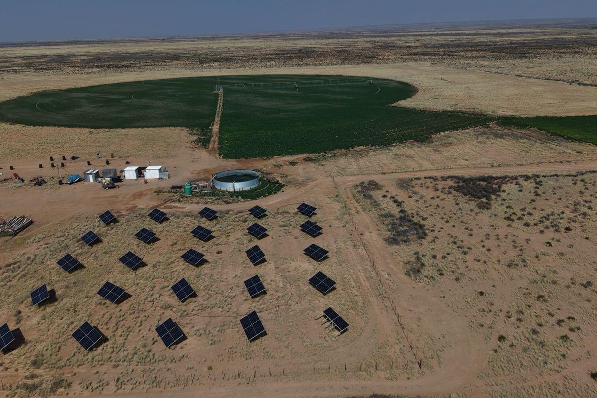 Aerial view of a farm featuring a solar panel array, a circular water reservoir, and a large center pivot irrigation system in the fields.