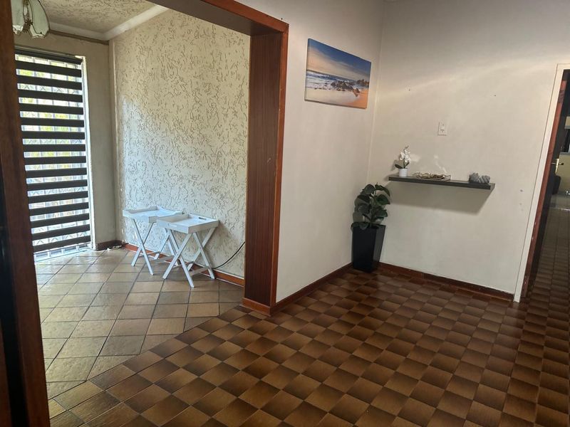 An entrance hall featuring dated tiled flooring, textured wall finishes, and a wooden door frame leading into the main living area.