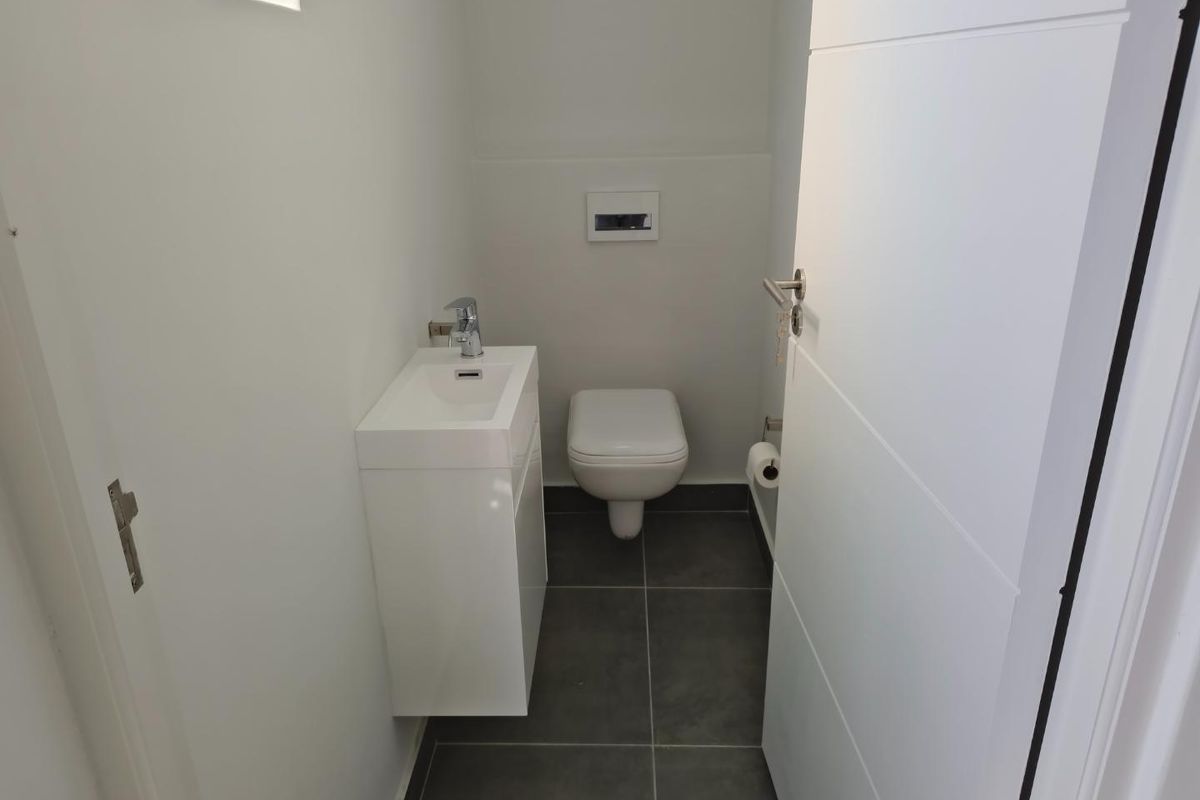 A modern, compact guest bathroom featuring a wall-mounted toilet, a sleek vanity basin, and dark floor tiling.