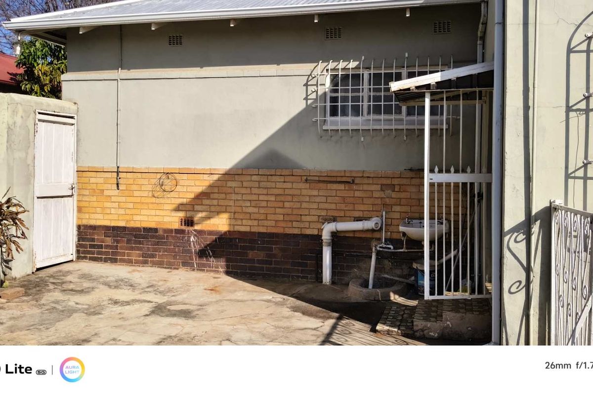 Rear exterior area featuring a concrete courtyard, brick facade, and external utility sink with security gate access.