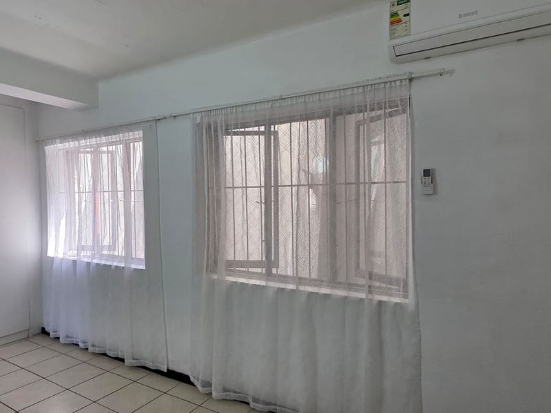 A bright, empty bedroom featuring tiled flooring, built-in cupboards, and a wall-mounted air conditioning unit.