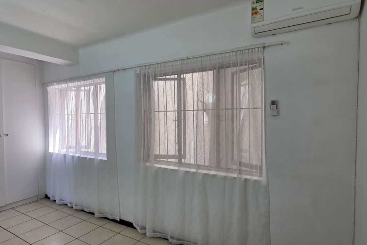 A bright, empty bedroom featuring tiled flooring, built-in cupboards, and a wall-mounted air conditioning unit.