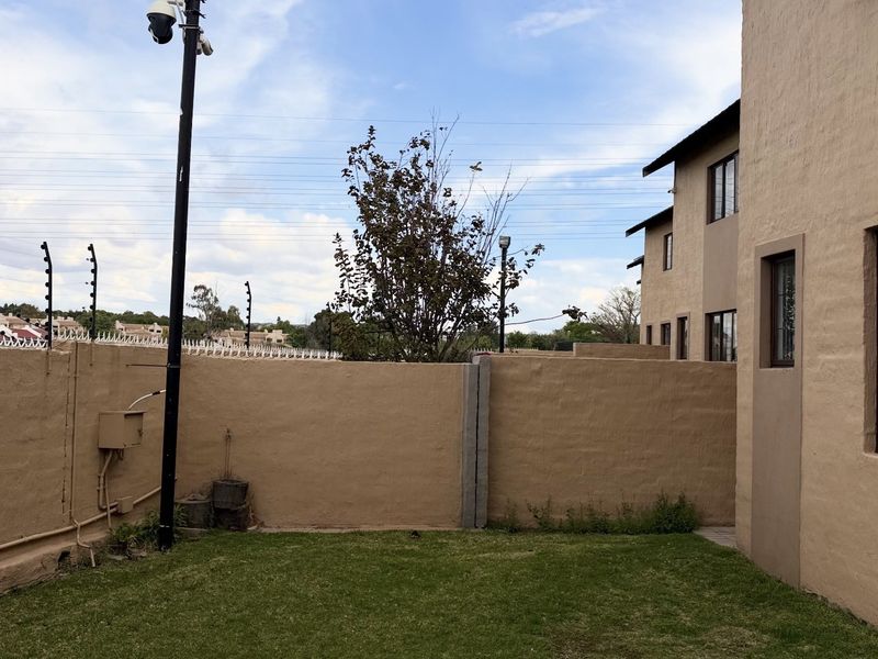 Rear garden area of the townhouse featuring a lawn, perimeter wall with electric fencing, and security camera installation.