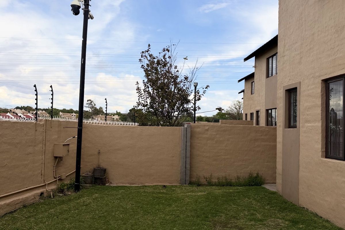 Rear garden area of the townhouse featuring a lawn, perimeter wall with electric fencing, and security camera installation.