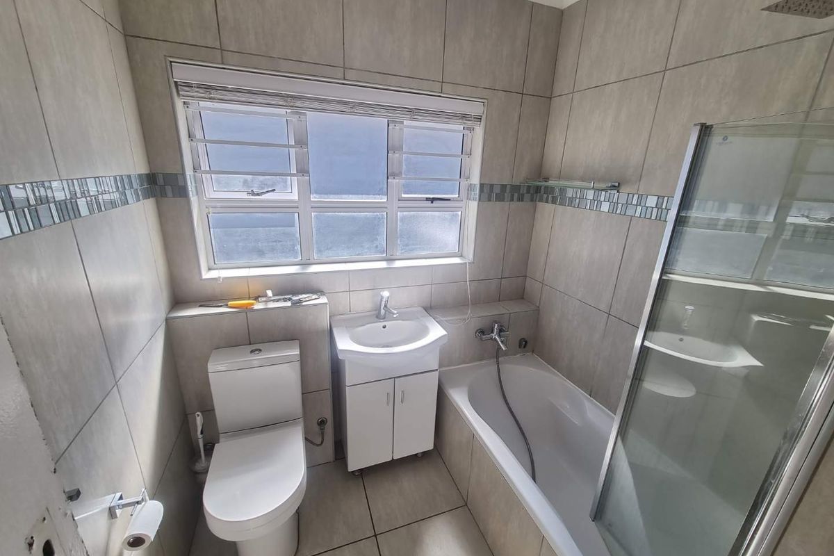A functional bathroom featuring a bathtub with a shower screen, a vanity basin, and a toilet, finished with neutral wall and floor tiles.