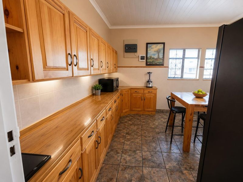 A functional kitchen featuring warm-toned wooden cabinetry, laminate countertops, tiled flooring, and a classic tongue and groove ceiling.