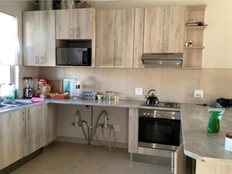 Functional kitchen featuring light wood-look cabinetry, built-in oven with hob, extractor fan, and stone-look countertops with an integrated sink.