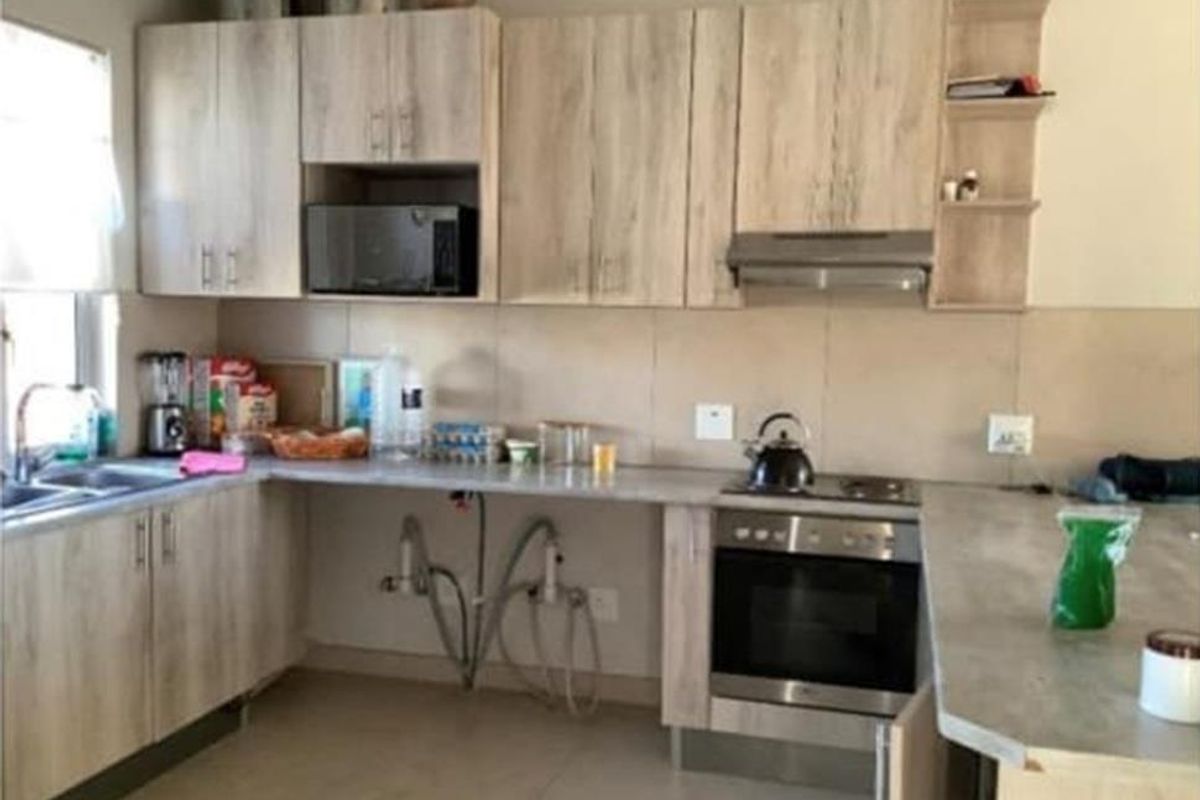 Functional kitchen featuring light wood-look cabinetry, built-in oven with hob, extractor fan, and stone-look countertops with an integrated sink.
