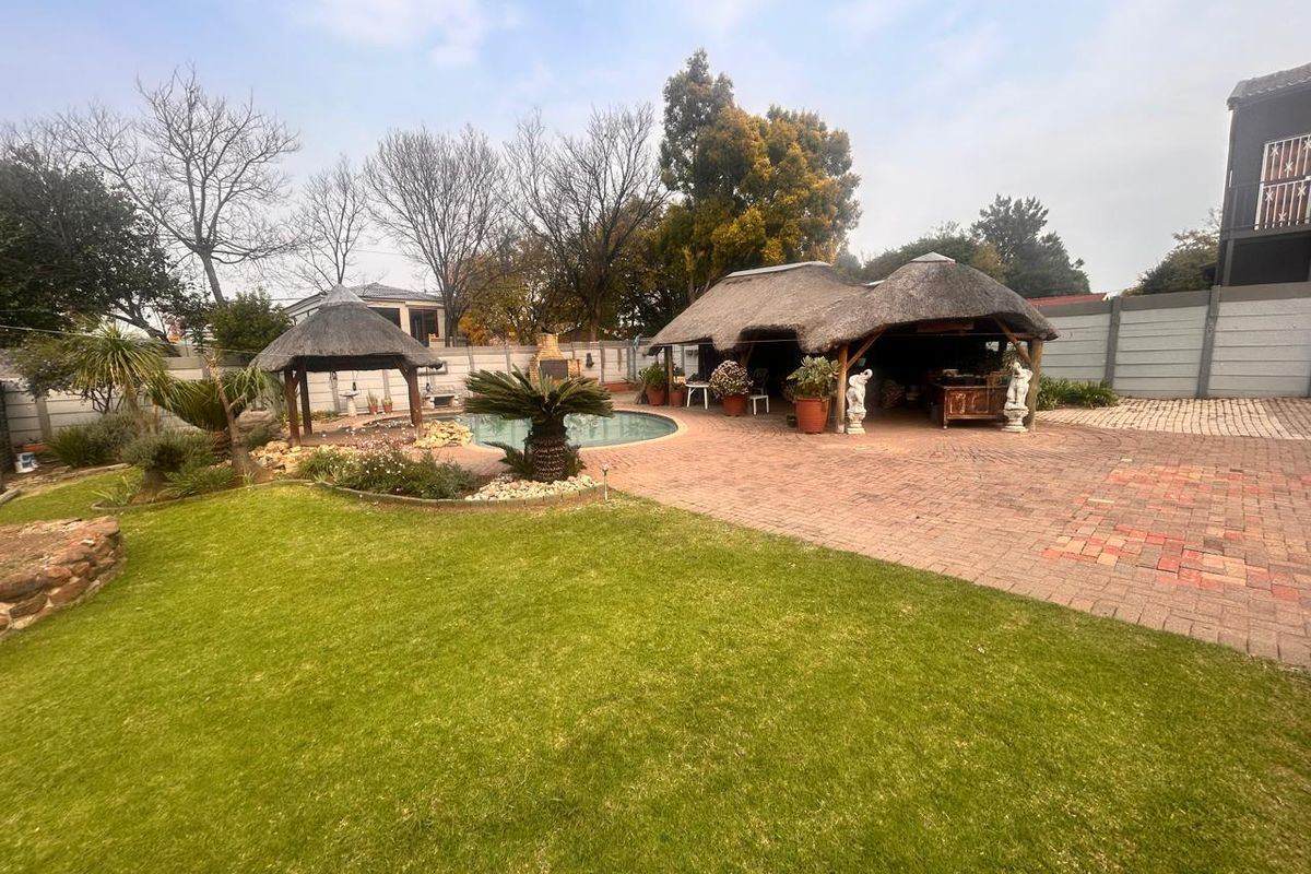 Spacious backyard featuring a swimming pool, a large thatched lapa entertainment area, a smaller gazebo, and established garden landscaping with paved surrounds.