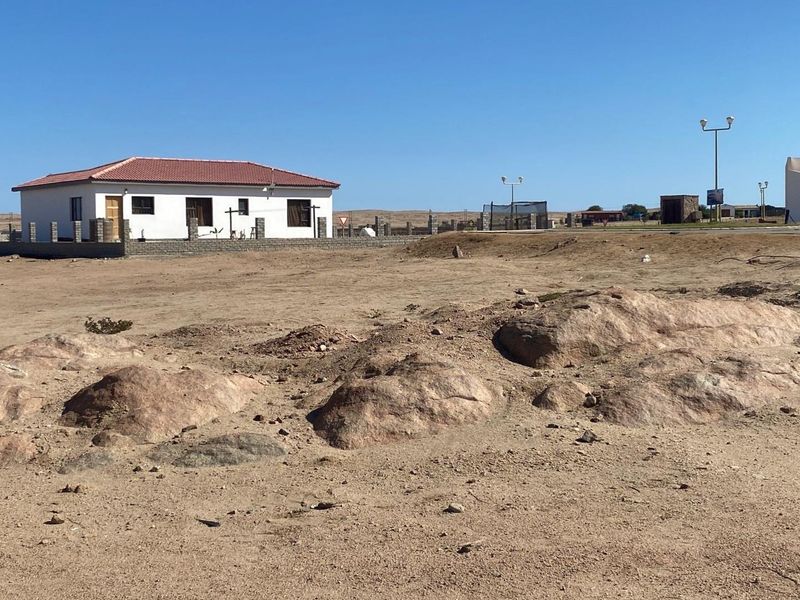 A view of a vacant residential plot featuring natural rocky terrain and surrounding boundary walls in a coastal development area.
