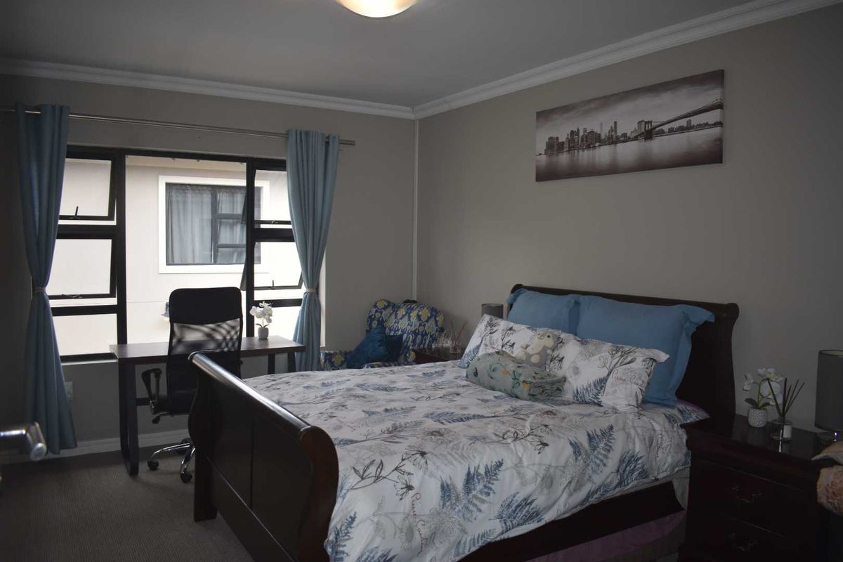 A well-lit bedroom featuring neutral wall tones, carpeted flooring, and large windows providing natural light.