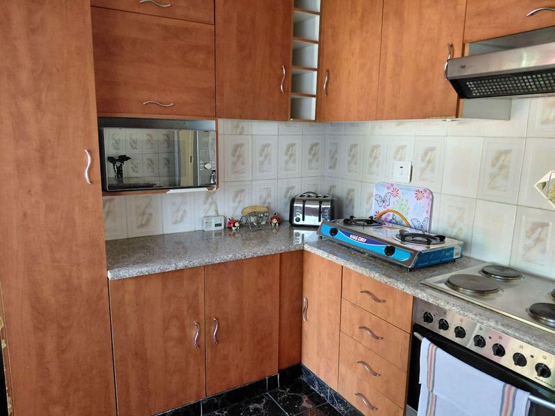 A functional kitchen featuring wood-tone cabinetry, granite countertops, a tiled backsplash, and integrated appliances including an oven, hob, and extractor fan.