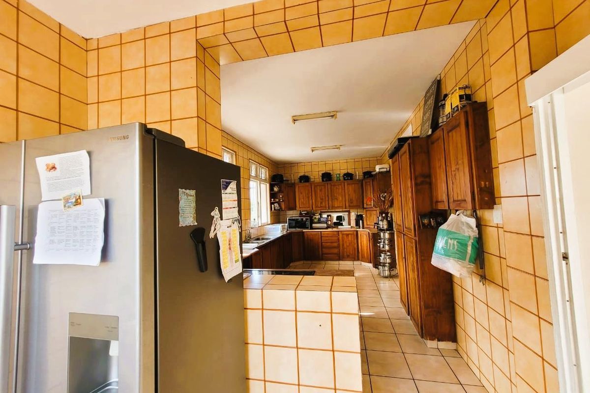 A spacious kitchen featuring extensive wooden cabinetry, tiled walls, and a functional layout with a breakfast counter area.
