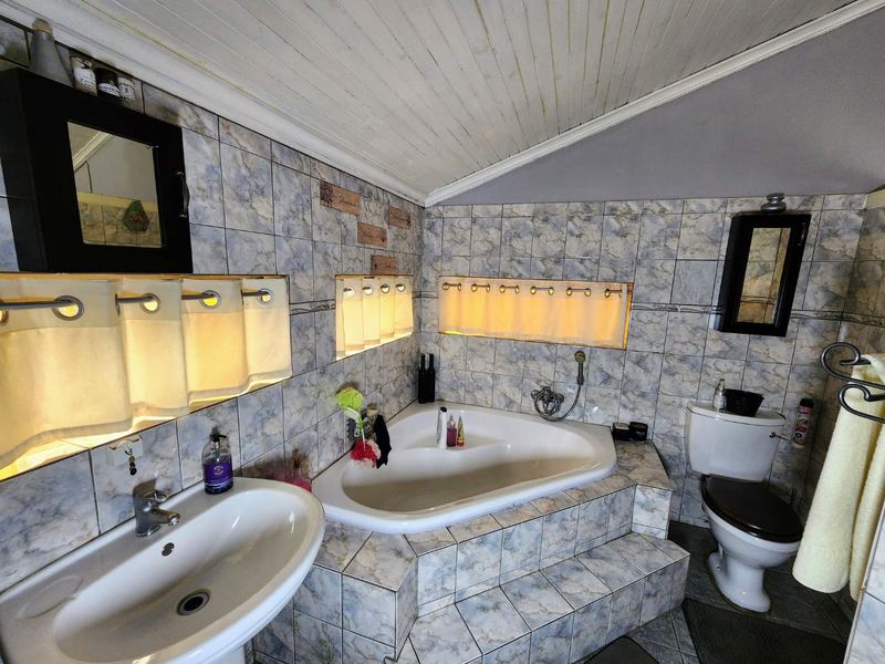 A dated bathroom featuring a corner bathtub, pedestal sink, toilet, and tiled surfaces with a sloped ceiling.